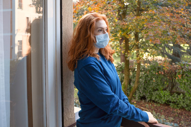 Jeune femme portant un masque et restant à la maison pour la pandémie covid-19 - Photo, image