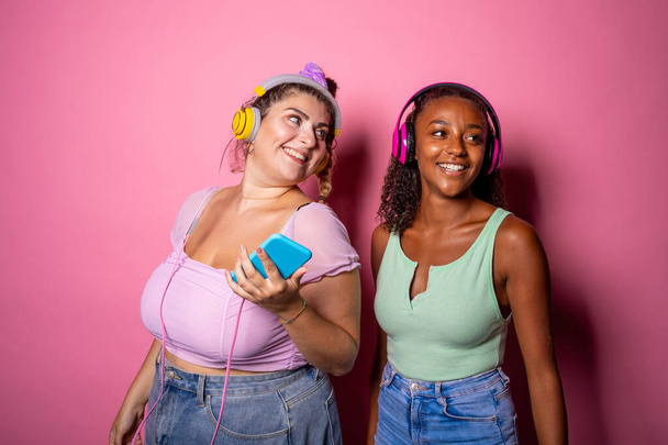 Ajustar y sobredimensionar adulto joven posando sobre fondo rosa escuchar música - Diversas mujeres con diferentes formas de cuerpo aisladas en el fondo - autoestima, autoaceptación, concepto positivo para el cuerpo - Foto, Imagen