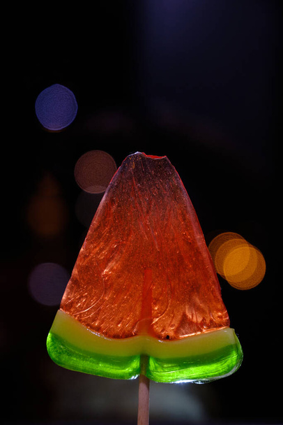 Γλυκιά φέτα, καρπούζι γλειφιτζούρι σε ένα μακρύ ραβδί με τη μορφή ενός τριγώνου, σε σκούρο φόντο - Φωτογραφία, εικόνα