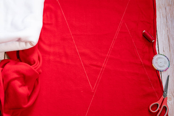 Master class on creating a red hat of Santa Claus. Blanks, fleece fabric, scissors, and a red spool of thread lie on a wooden table. Step by step instructions. Step 2. - Fotoğraf, Görsel