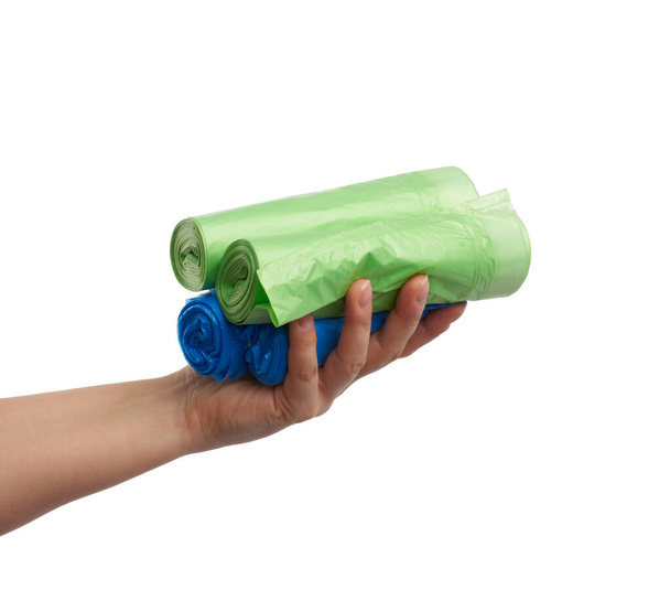 жіноча рука тримає пучок синіх і зелених поліетиленових пакетів для сміття, частина тіла з предметом ізольована на білому тлі
 - Фото, зображення