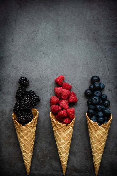 Bagas frescas em cones de waffle no fundo de pedra escura, vista superior. Conceber comida saudável e deserto. Espaço de cópia. - Foto, Imagem