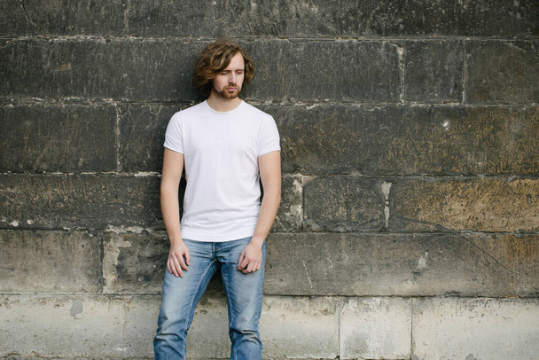 Hipster handsome male model wearing white blank t-shirt with space for your logo or design in casual urban style on europian streets - Foto, Imagem