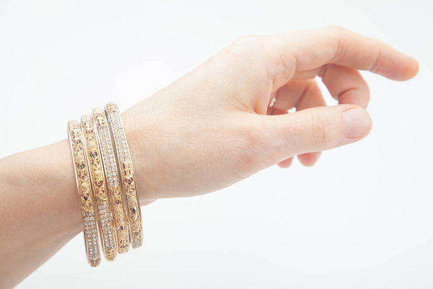 Vrouwelijke hand met set van gouden armbanden op witte achtergrond met selectieve focus - Foto, afbeelding