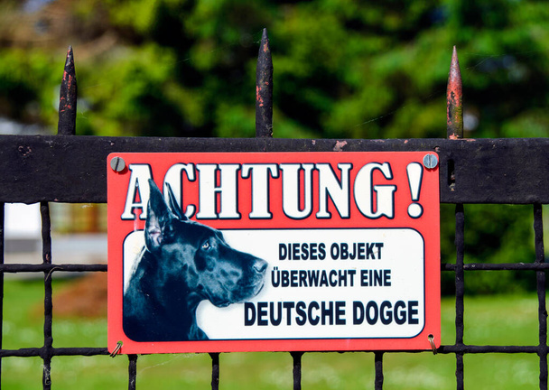 Warntafel mit dem Text "Achtung! Dieses Objekt wird von einer Deutschen Dogge "auf einem eisernen Zaun beobachtet - Foto, Bild