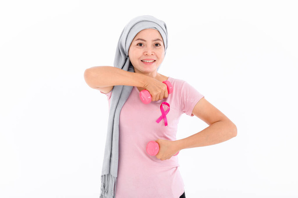 Ασιάτισσες μουσουλμάνες με χιτζάμπ δένουν μια ροζ κορδέλα στις κορυφές τους. Ασκείται σηκώνοντας ροζ αλτήρες. έννοια του καρκίνου του μαστού, την πρόληψη του καρκίνου. Ακμή και σκοτεινά σημεία. - Φωτογραφία, εικόνα