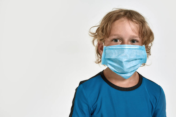 Close up portrait of little sportive boy child in sportswear wearing medical mask, looking at camera while posing, standing isolated over white background - Foto, Imagem