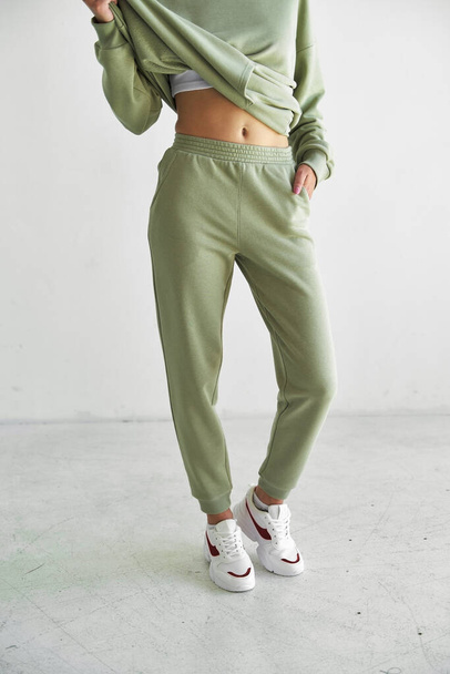 sporty young girl wears green sporty pants. fit woman stands in studio - Photo, Image