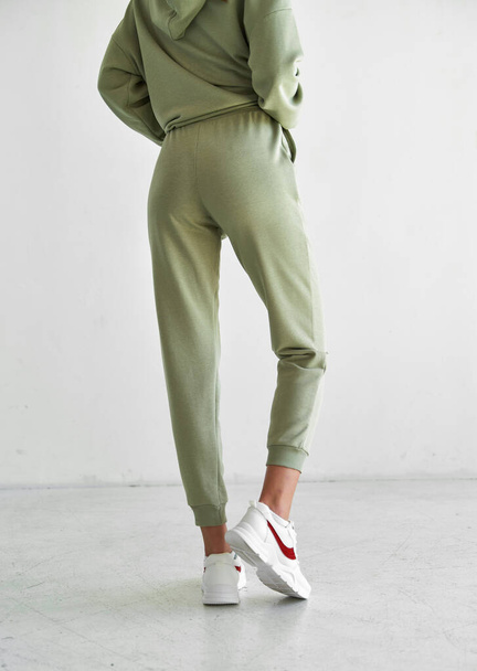 chica joven y deportiva lleva pantalones deportivos verdes. mujer en forma se para en estudio - Foto, imagen