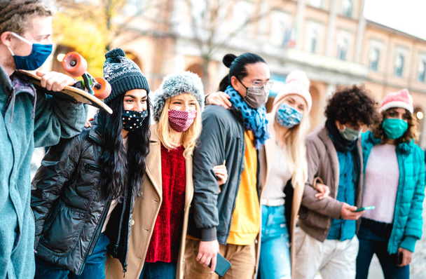 Milenyum insanları birlikte yürüyüp, şehir merkezinde yüz maskesi takarak eğleniyorlar. Kış kıyafetleri giymiş çok kültürlü arkadaşlarla yeni normal arkadaşlık kavramı. Parlak canlı filtre. - Fotoğraf, Görsel