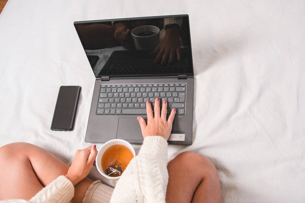 дівчина працює вдома комфортно з ліжка або дивана з чашкою чаю під час пандемії вірусу
 - Фото, зображення