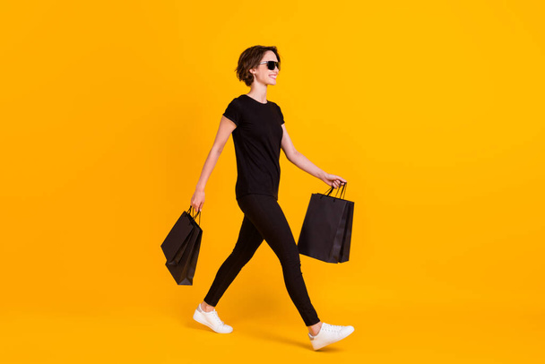 Full length body size profile side view of attractive skinny cheerful girl going carrying packages isolated bright yellow color background - Fotografie, Obrázek