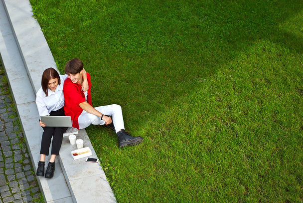 Boy and girl have lunch outdoors together. Couple looking at laptop screen. The concept of fast food and street food. Food in paper containers and disposable cups. - Foto, Imagen