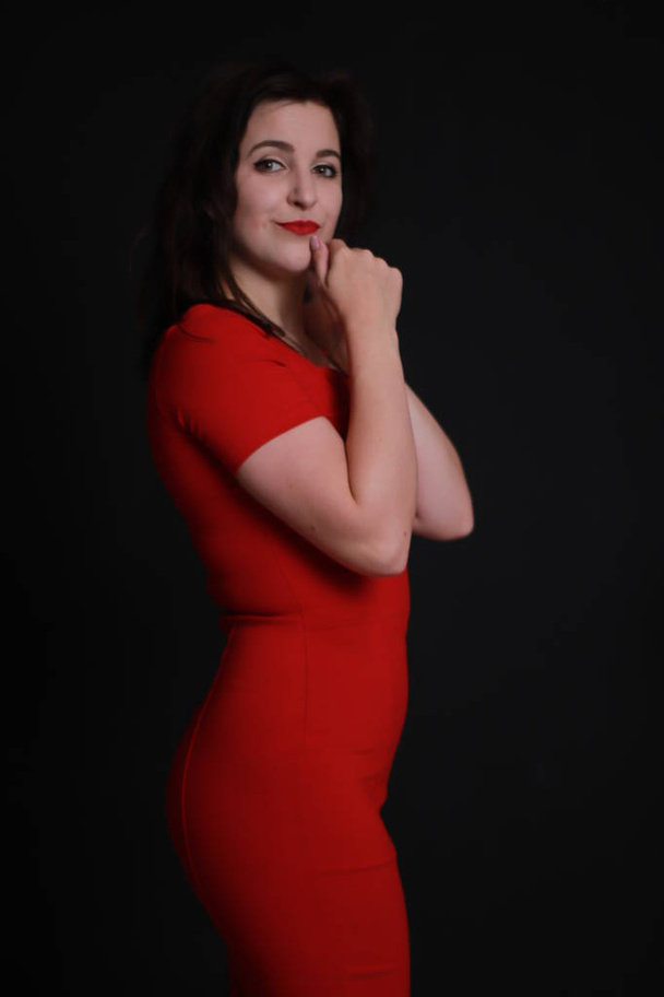 黒い背景に隔離された赤いスキニードレスのセクシーな魅力的なブルネット。スタジオ撮影。感情的な女優.  - 写真・画像