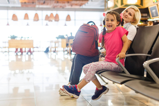 Мама и ребенок ждут свой самолет в аэропорту. Пассажиры ждут свой транспорт на вокзале - Фото, изображение