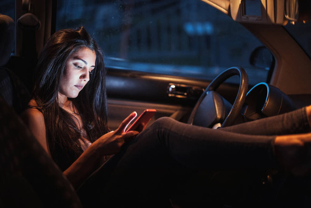 Γυναίκα μέσα σε ένα αυτοκίνητο χρησιμοποιώντας το smartphone της κοιτάζοντας μέσα από το παράθυρο - Φωτογραφία, εικόνα