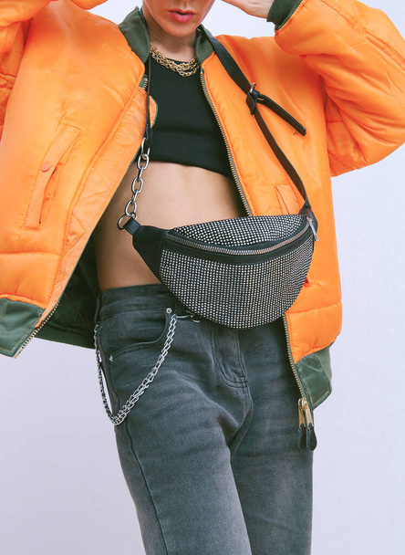 Model in fashion urban street outfit. Trendy orange bomber jacket and stylish clutch bag. Fall winter seasons lookbook. Style in details - 写真・画像