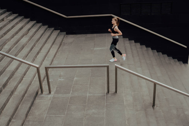 A young girl in a tracksuit runs up the stairs, in a business center - Foto, imagen