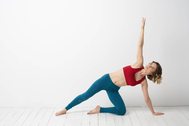 Eine Frau in blauen Jeans praktiziert Yoga vor hellem Hintergrund drinnen und eine schlanke Figur beim Turnen - Foto, Bild