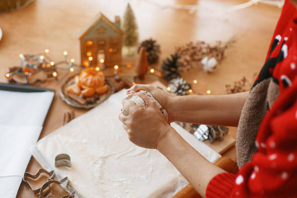 Руки разминают сырое пряничное тесто на фоне металлических резаков, специй, апельсинов, праздничных украшений на деревенском столе. Человек, который делает пряничное печенье, рождественская традиция - Фото, изображение