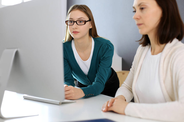 Businesswoman giving presentation to her female colleague while they sitting at the desk with computer. Group of business people working in office. Teamwork concept - Photo, Image