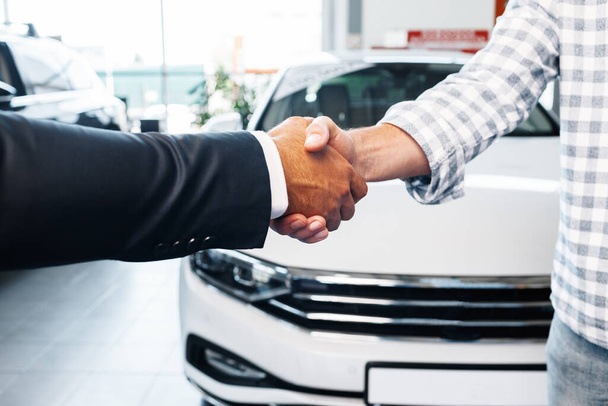 Customer shaking hands with professional car dealer at automobile dealership - Foto, Bild