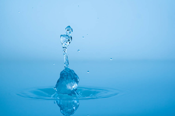 Water drop splashing into blue water surface - Fotó, kép