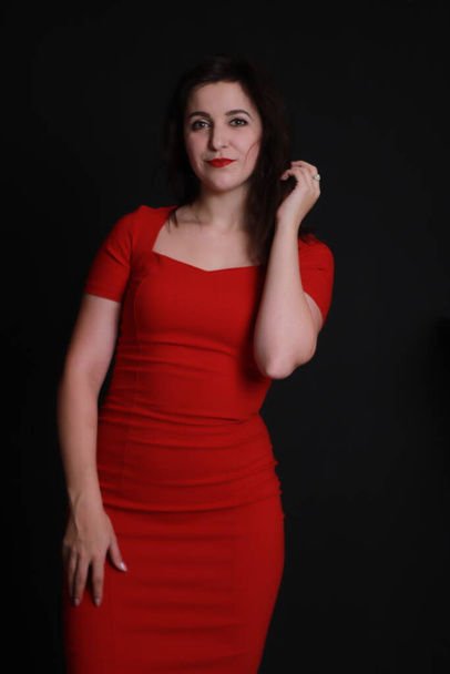 σέξι ελκυστική μελαχρινή σε κόκκινο κοκαλιάρικο φόρεμα απομονώνονται σε μαύρο φόντο. Φωτογράφηση στούντιο. συναισθηματική ηθοποιός.  - Φωτογραφία, εικόνα