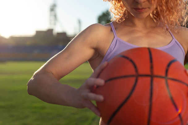 dziewczyna sportowiec biketball gracz, trzymając piłkę w ręku, na tle zachodzącego słońca. Na zewnątrz Konkurencyjny koszykarz trzymający piłkę - izolowany na czarnym tle - Zdjęcie, obraz