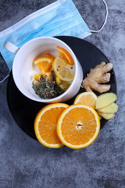 Tazza di tè bianco con limone, zenzero, arancia., marmellata e maschera medica sullo sfondo grigio scuro. Sanita '. Cocktail di vitamine. - Foto, immagini