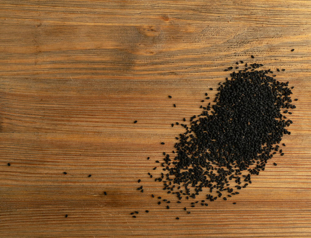 Czarny kminek lub czarny kminek pikantne nasiona na tle drewna widok z góry. Nigella sativa znana również jako makieta nigella, kalojeere i kalonji - Zdjęcie, obraz