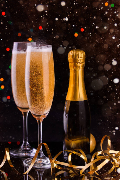 Zwei Gläser mit Champagner und einer Flasche Champagner, Lichter, seitlich, Serpentinen. Neujahrsinhalt 2021. Dunkler Hintergrund - Foto, Bild
