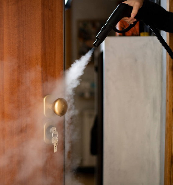 desinfectie en ontsmetting met stoom thuis, stoomstroom is gericht op de deurkruk en sleutels in het slot - Foto, afbeelding