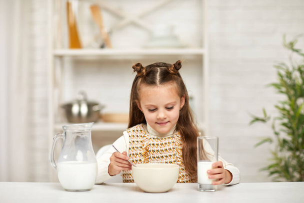 little girl eating breakfast: cereal with the milk in the kitchen. - Fotó, kép