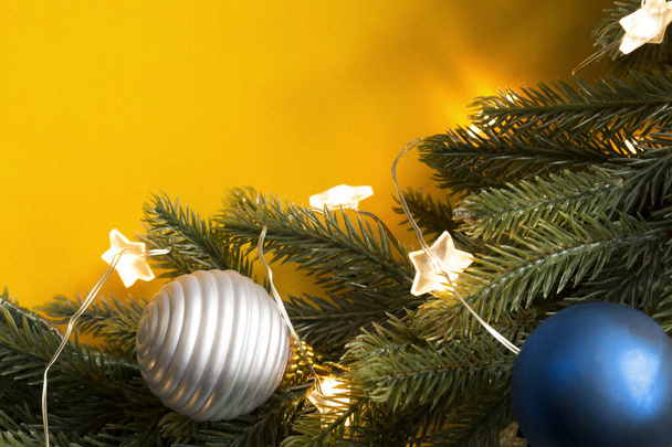 Christmas tree branch with balls and lights closeup on yellow background - Φωτογραφία, εικόνα