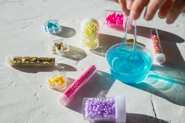 Criança segurando Ingredientes, garrafas, frascos para fazer um brinquedo popular das crianças da cola. Caseiro rosa, amarelo, branco lodo da moda com bolas para entretenimento e hobbies em caixas redondas. - Foto, Imagem
