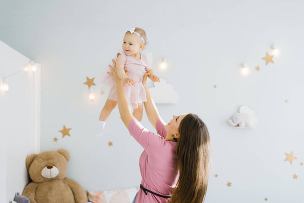 A mother and a small child play in the children's room. happy family relationships. Mom throws up a happy one-year-old daughter. - Photo, Image