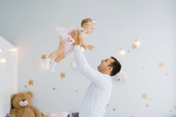 Father lifting baby girl. Happy father picks up and throws his lifting a small child. Home atmosphere, happy family laughing baby - Photo, Image