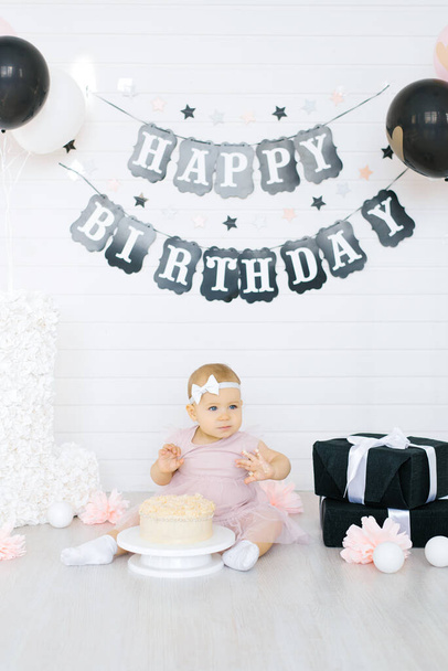 Célébrer le premier anniversaire d'une petite fille. Un enfant s'assoit près d'un gâteau dans une zone photo festive - Photo, image