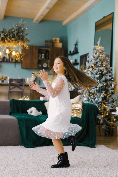 Una ragazza si diverte e balla in un elegante salotto in stile scandinavo decorato per Natale - Foto, immagini