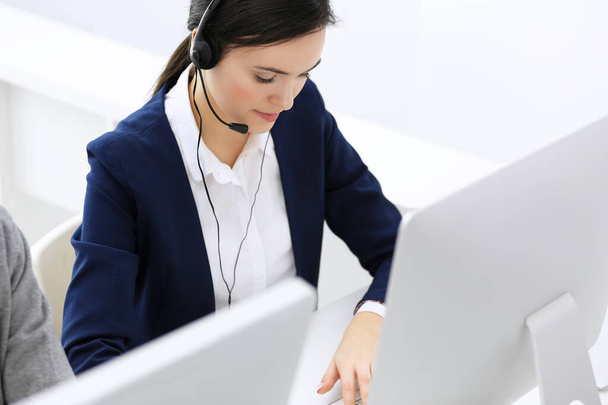 Call center. Beautiful woman receptionist sitting in headset at customer service office. Group of operators at work. Business concept - Photo, image