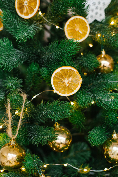 Рождественская елка украшена игрушками, сушеными лимонами или апельсинами, золотыми шариками, белыми яйцами и гирляндами крупным планом. - Фото, изображение