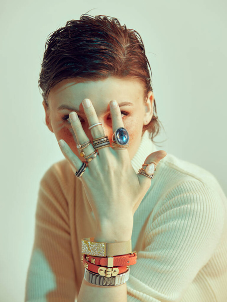 Female hand with rings and bracelets covers young face of redhead stylish girl with short hair, studio portrait - Foto, imagen