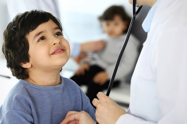 Arzt untersucht eine Kinderpatientin mit einem Stethoskop. Netter arabischer Junge beim Arzttermin. Medizin und Gesundheitskonzept - Foto, Bild