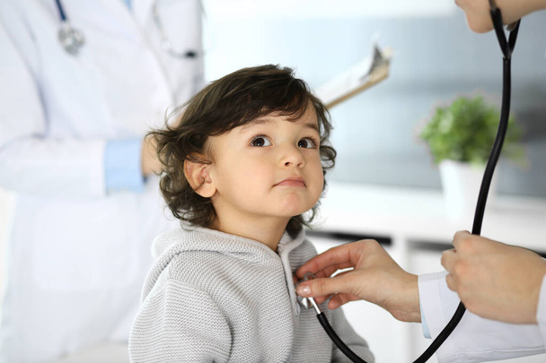 Doctor examining a child patient by stethoscope. Cute arab boy at physician appointment. Medicine and healthcare concept - Фото, зображення