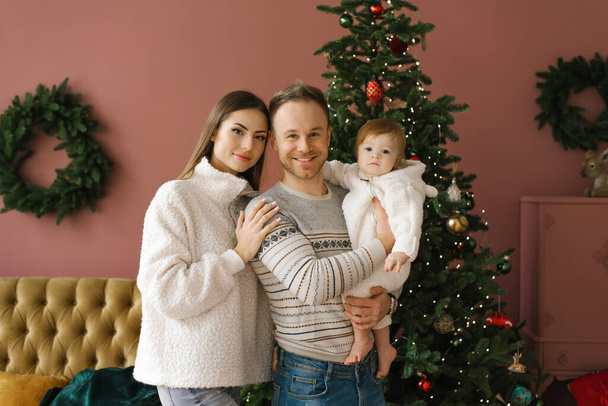 新しい家のリビングルームでクリスマスツリーの近くに小さな子供を持つスタイリッシュな若い家族の家族の肖像画 - 写真・画像