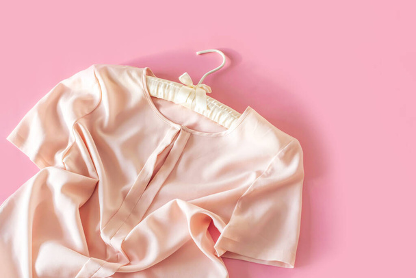Розовая женщина блузка висит на красивой вешалке на розовом фоне с копировальным пространством. Концепция продажи и покупок. - Фото, изображение