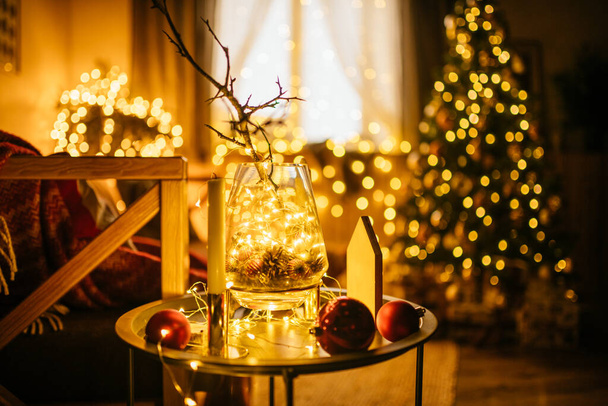 New Year 2021 interior with candles, bulbs and bokeh. Room decorated to christmas celebration. Christmas tree with presents - Фото, изображение