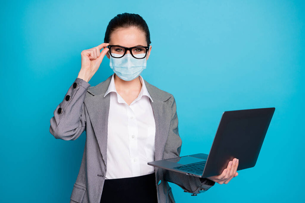 Portrait of nice cheerful skilled lady IT expert holding in hand laptop wear mask isolated over bright blue color background - Foto, imagen