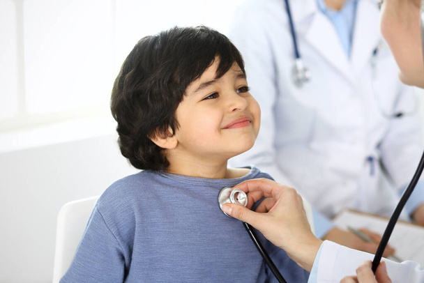 Doctor examining a child patient by stethoscope. Cute arab boy at physician appointment. Medicine and healthcare concept - Fotografie, Obrázek